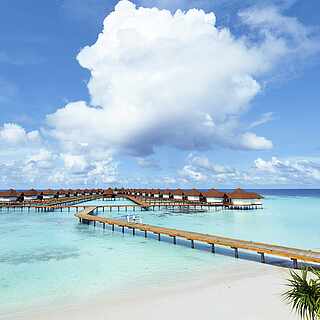 Steg über einen paradiesischen Strand ins Wasser hin zu kleinen Hütten auf dem Meer